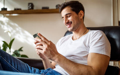 Mann sitzt entspannt mit Handy in Sessel und stellt seine Smartphone-Daten wieder her