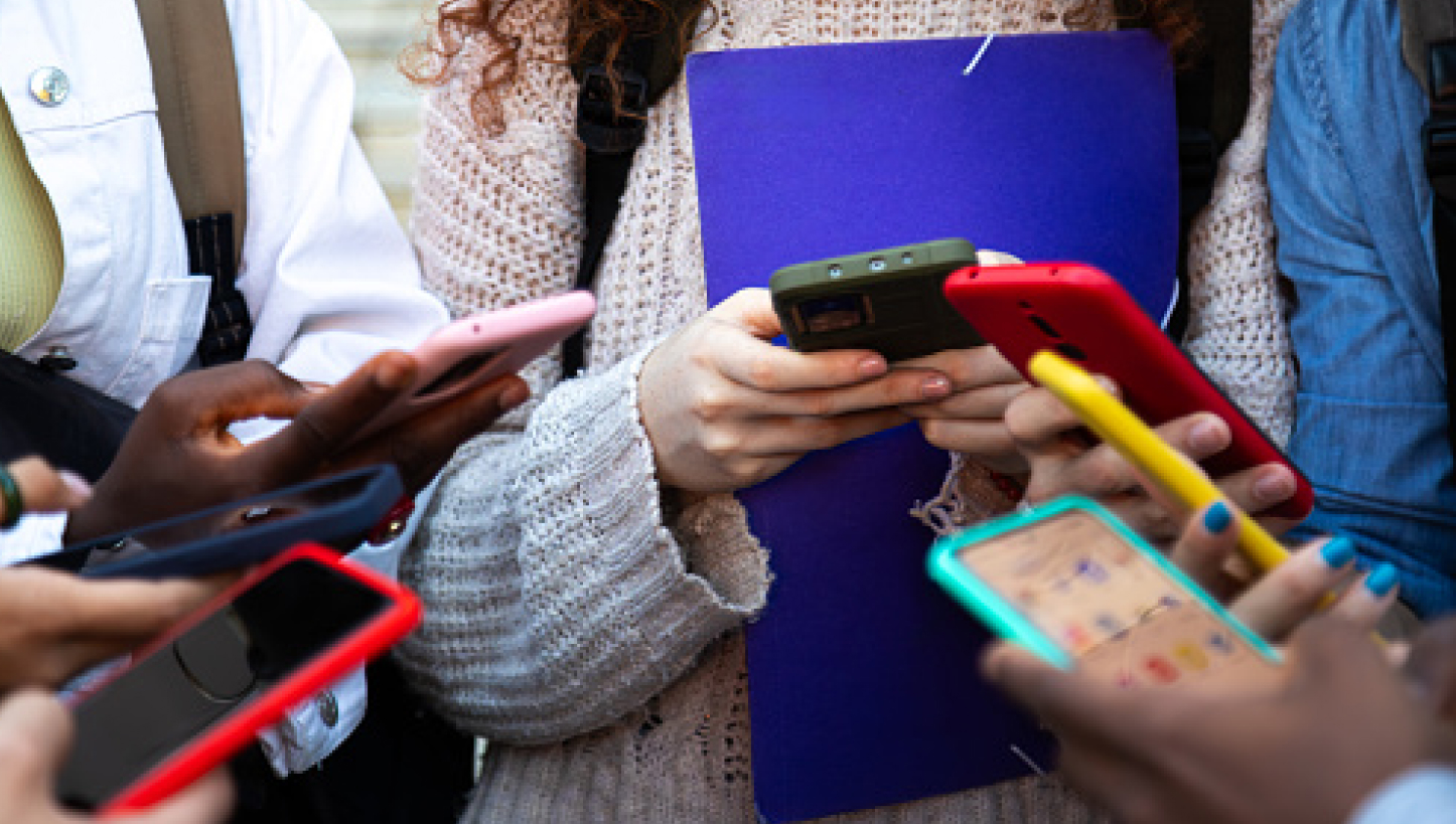 Junge Leute stehen im Kreis und schauen auf ihre farbigen Smartphones.